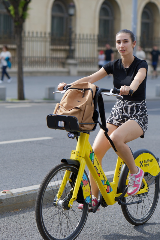 19 - Girl on a yellow I'Velo bike-sharing bicycle featuring a front storage basket and a brightly colored graphic on its frame